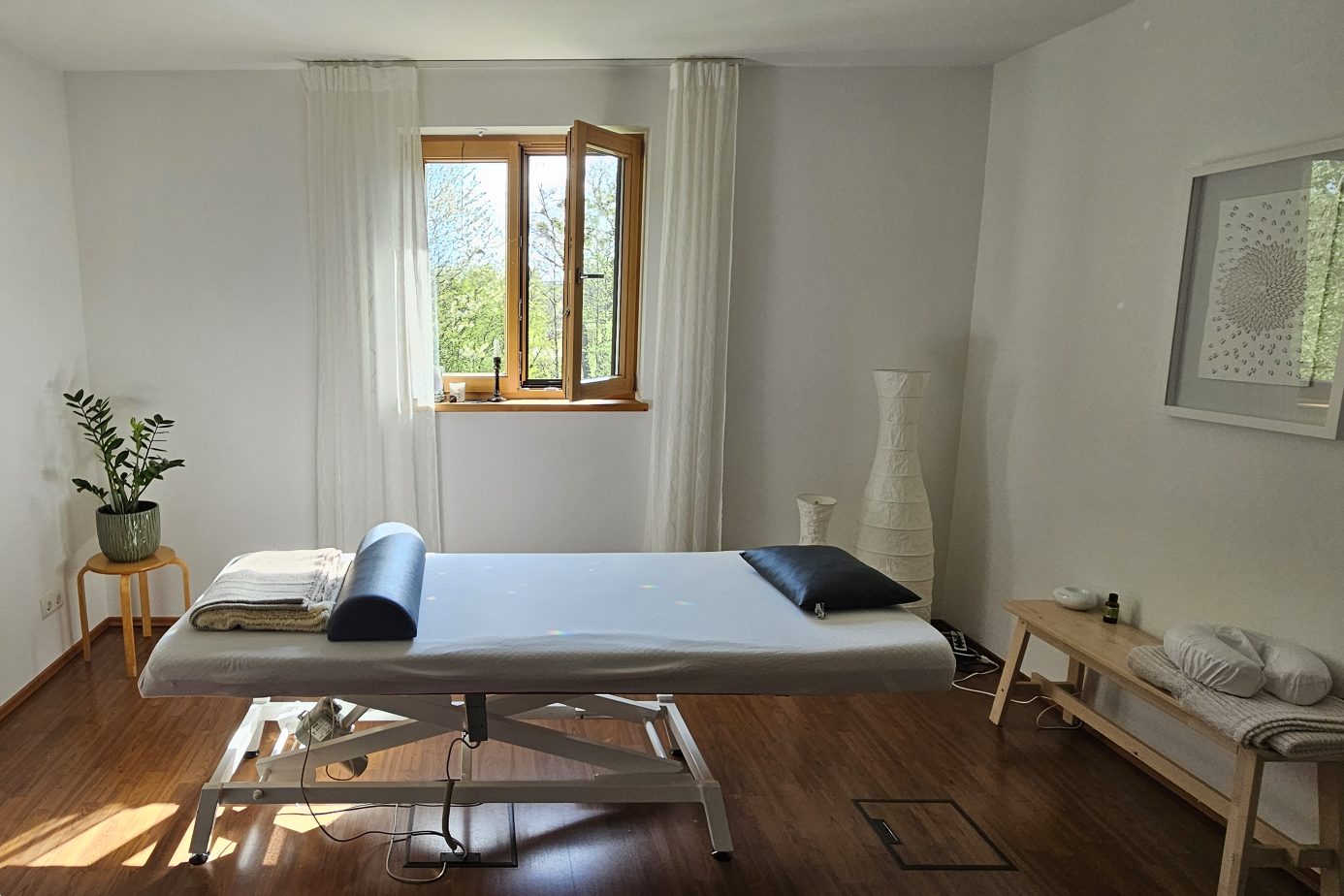 Behandlungsraum der Naturheilpraxis mit Behandlungsliege und Blick ins Grüne